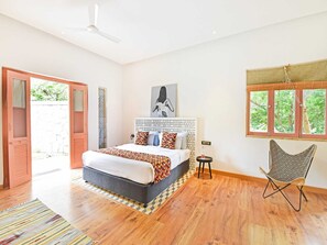 Un dormitorio con cama, una silla, un ventanal y una puerta.