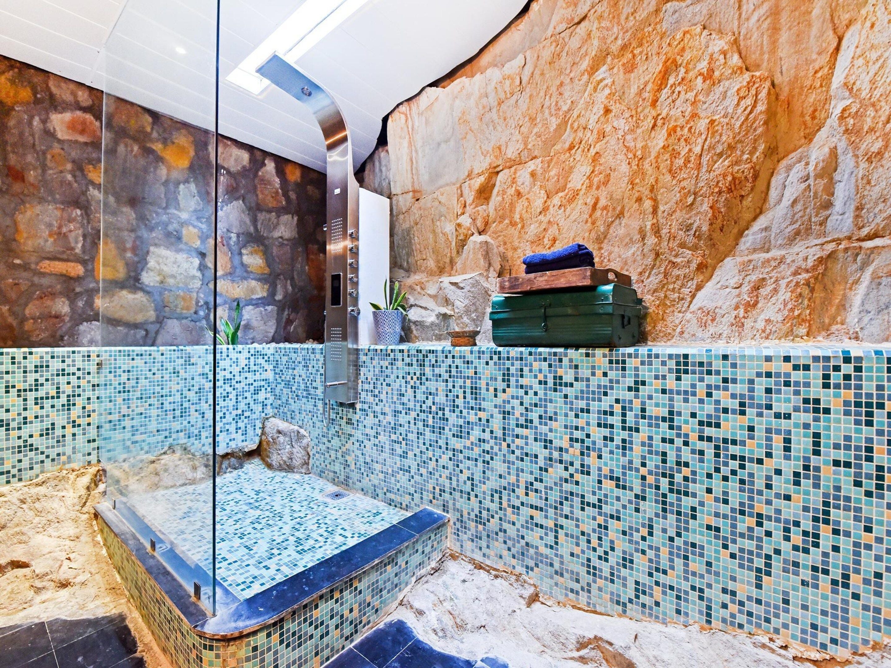 A bathroom with a stone wall, a tiled floor, and a glass shower enclosure.
