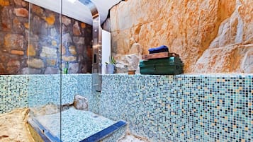 A bathroom with a stone wall, a tiled floor, and a glass shower enclosure.