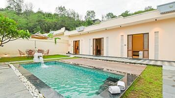 Un área de piscina exterior moderna con superficie de agua cristalina, rodeada por un borde de piedra y contigua a un edificio de techo plano y amplios ventanales.