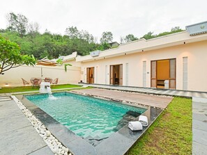 Un área de piscina exterior moderna con superficie de agua cristalina, rodeada por un borde de piedra y contigua a un edificio de techo plano y amplios ventanales.