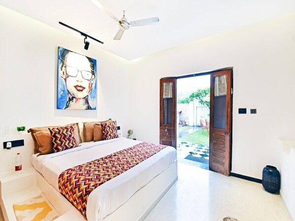 A bedroom with a bed, a ceiling fan, a door leading outside, and a painting on the wall.