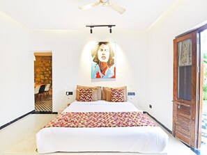 Un dormitorio con cama, ventilador de techo, un cuadro y una puerta que da a un balcón.