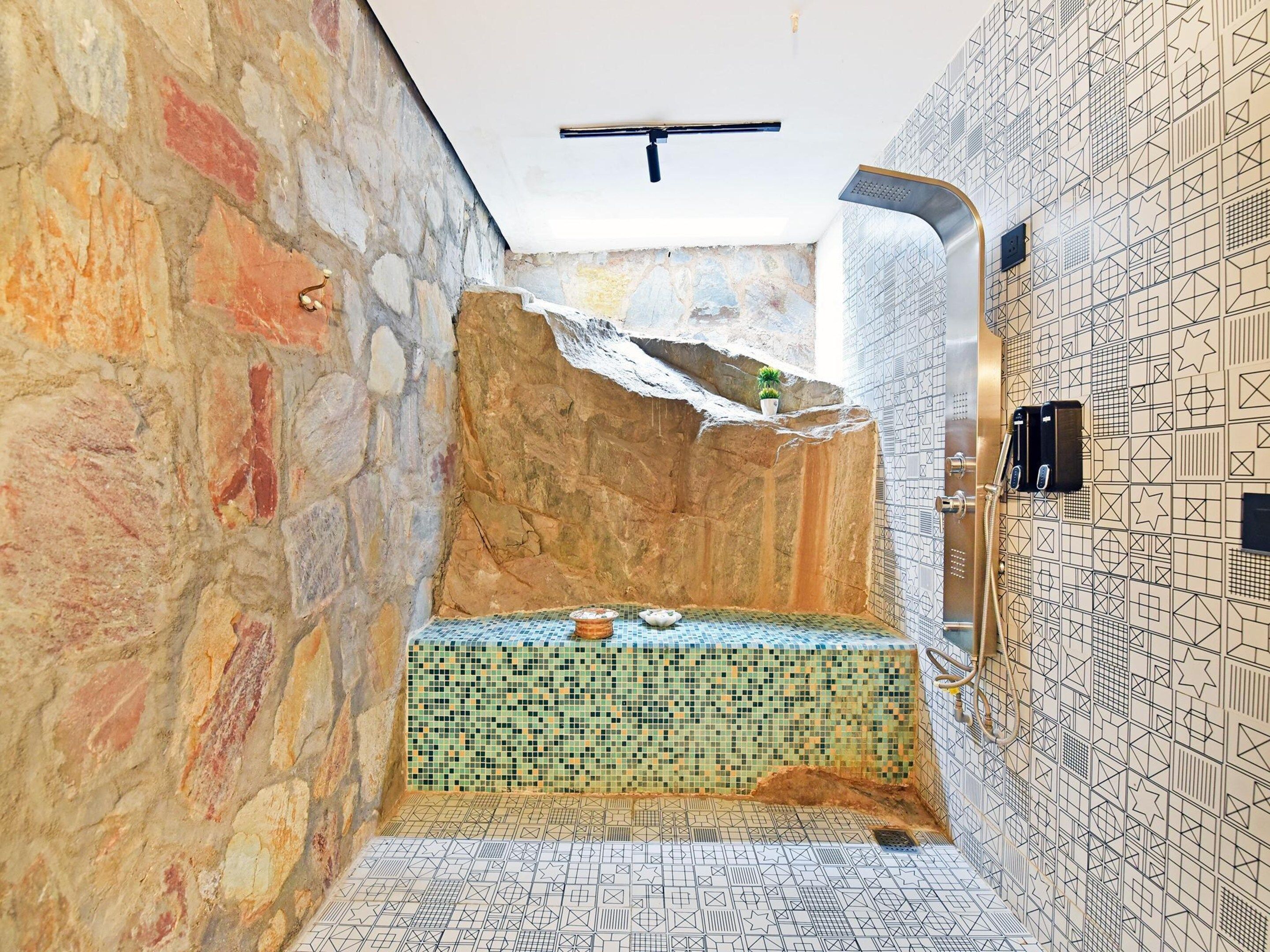 Ein Badezimmer mit Steinwand, Fliesenboden und Duschbereich.