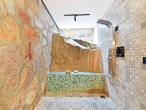 Un baño con pared de piedra, piso de baldosas y zona de ducha.