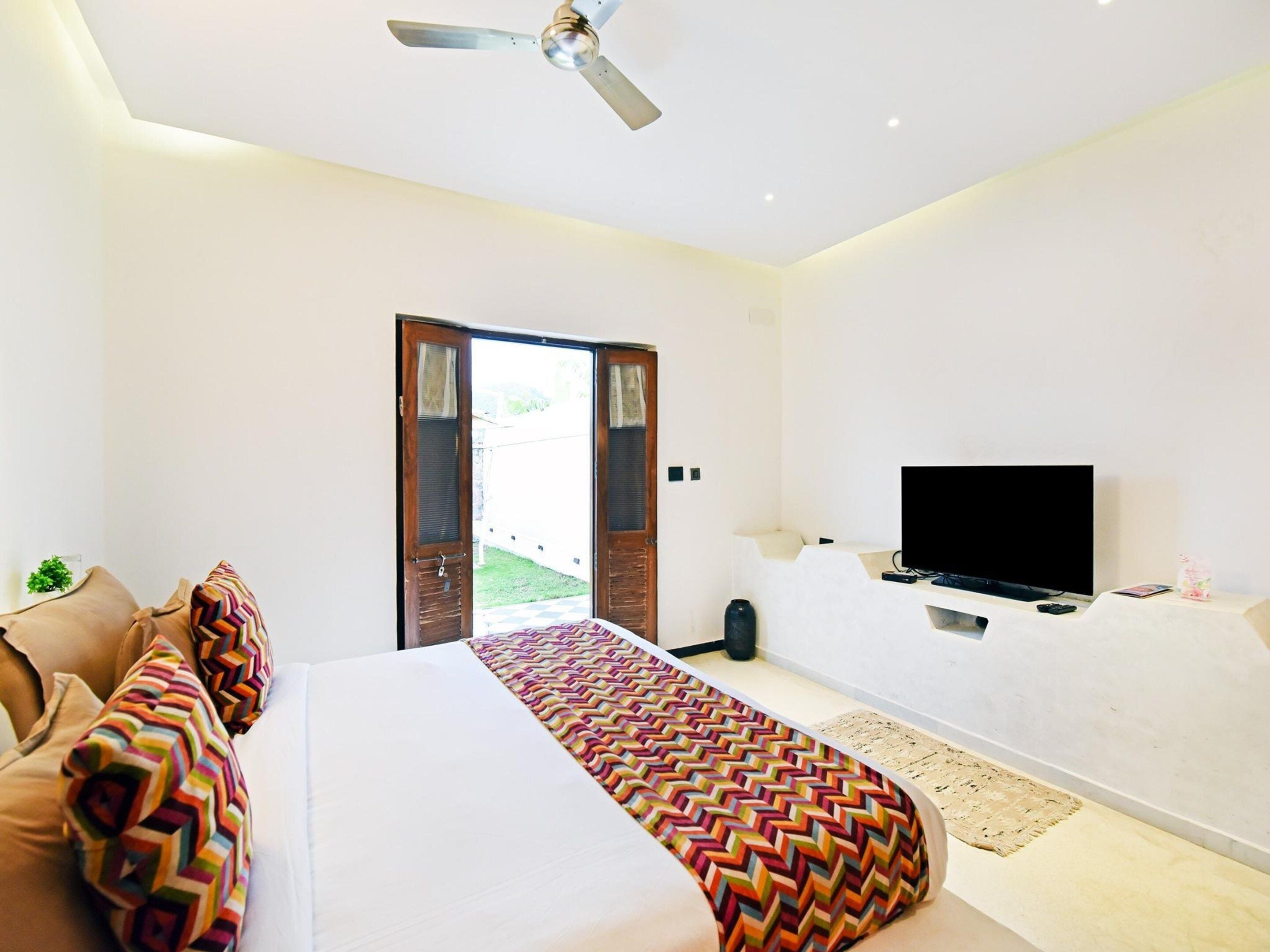 A hotel room with a bed, a television, and a door leading to an outdoor area.