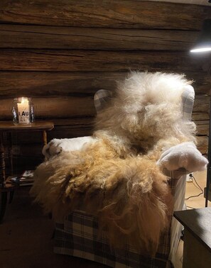 A plush, white, furry chair with a plaid base in a room with wooden walls and a lit candle on a side table.