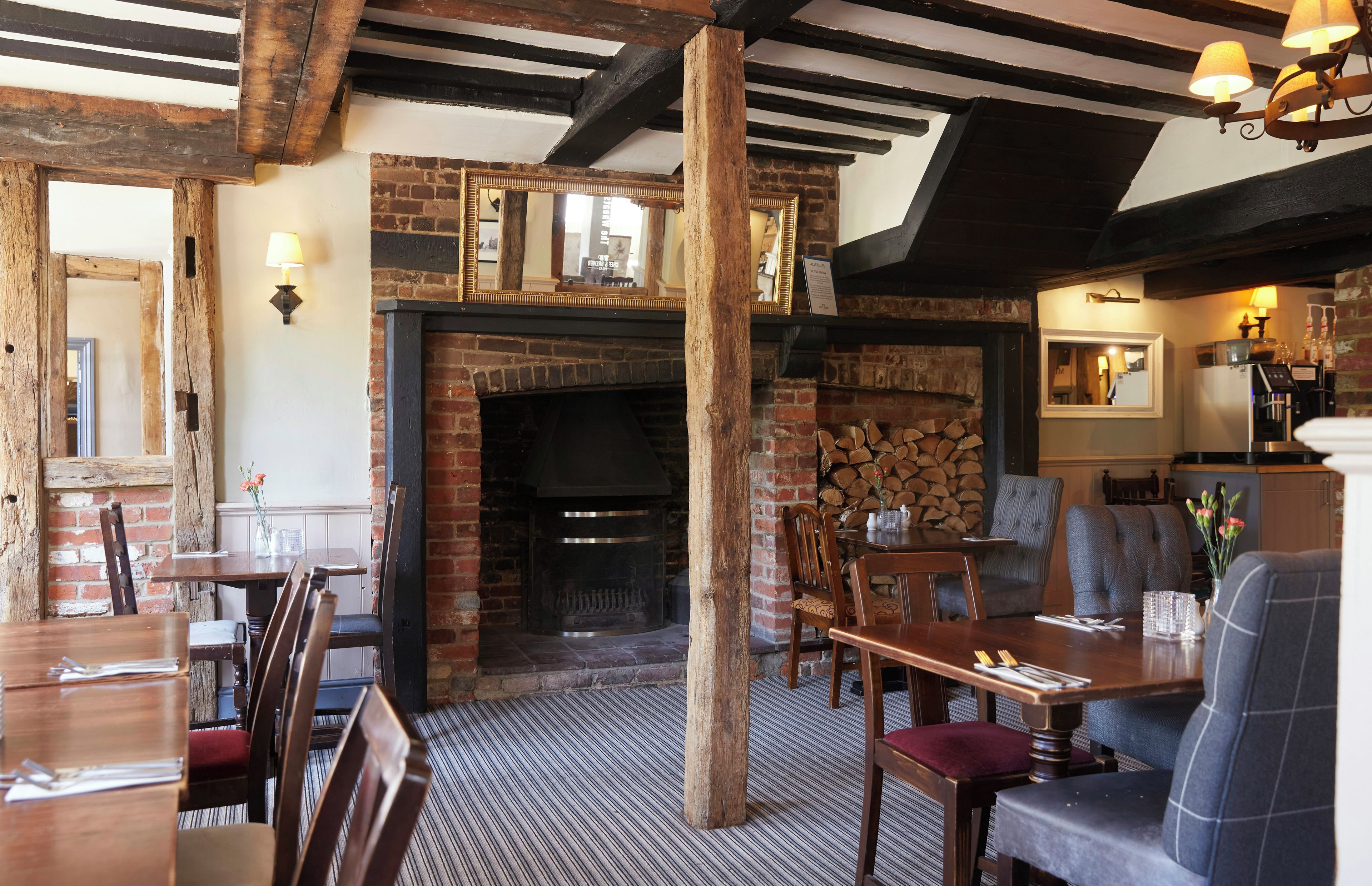 A rustic interior with exposed wooden beams, a brick fireplace, and a seating area with tables and chairs.