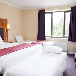 A hotel room with two beds, a window with curtains, a nightstand, and a wall-mounted lamp.