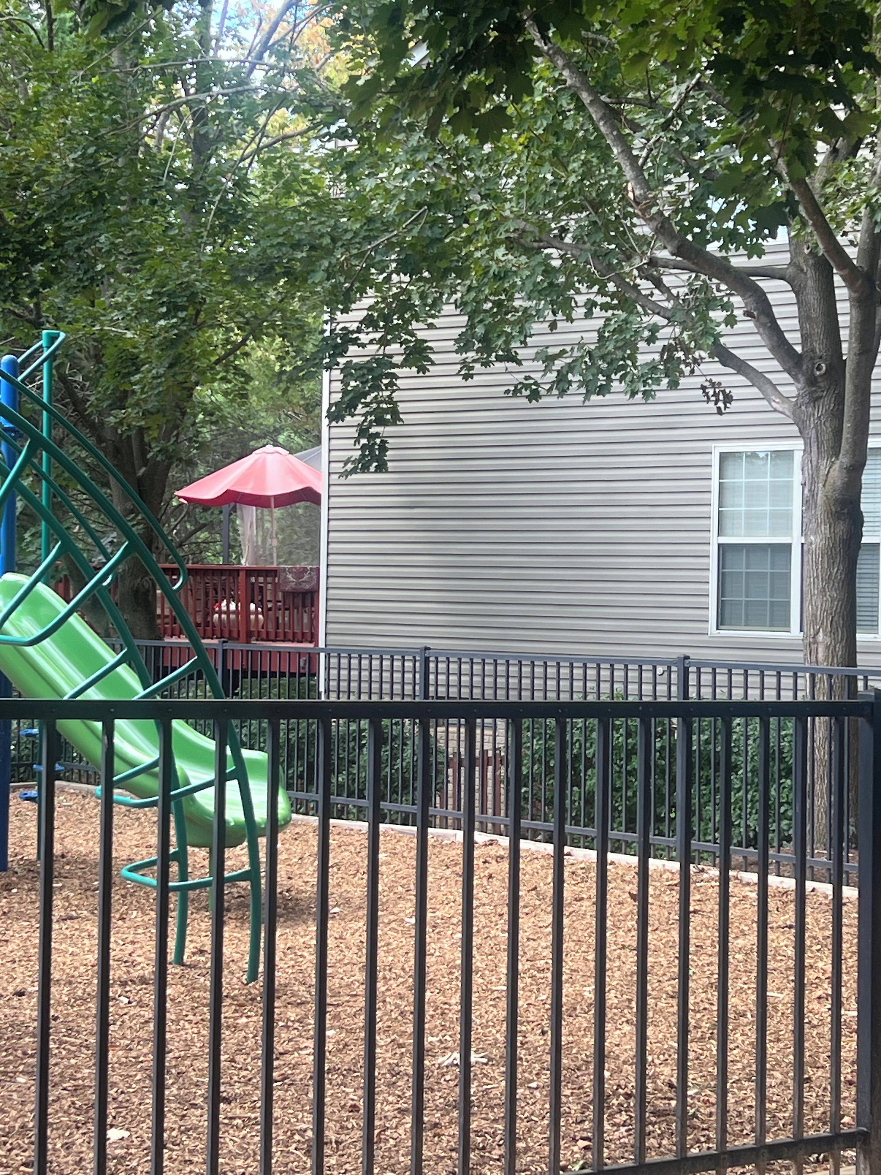 A fenced playground area with a green slide and a red umbrella.