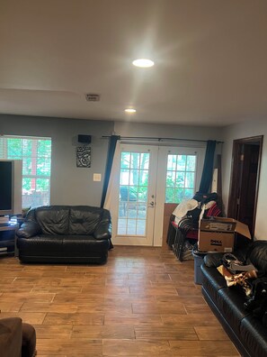 A living room with a black leather sofa, wooden flooring, a television, and a door leading outside. - Cozy 1-bedroom house in perfect Manassas with AC (Manassas)