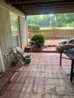 A covered patio area with a brick floor, a small green planter, and a wooden fence in the background. - Cozy 1-bedroom house in perfect Manassas with AC (Manassas)