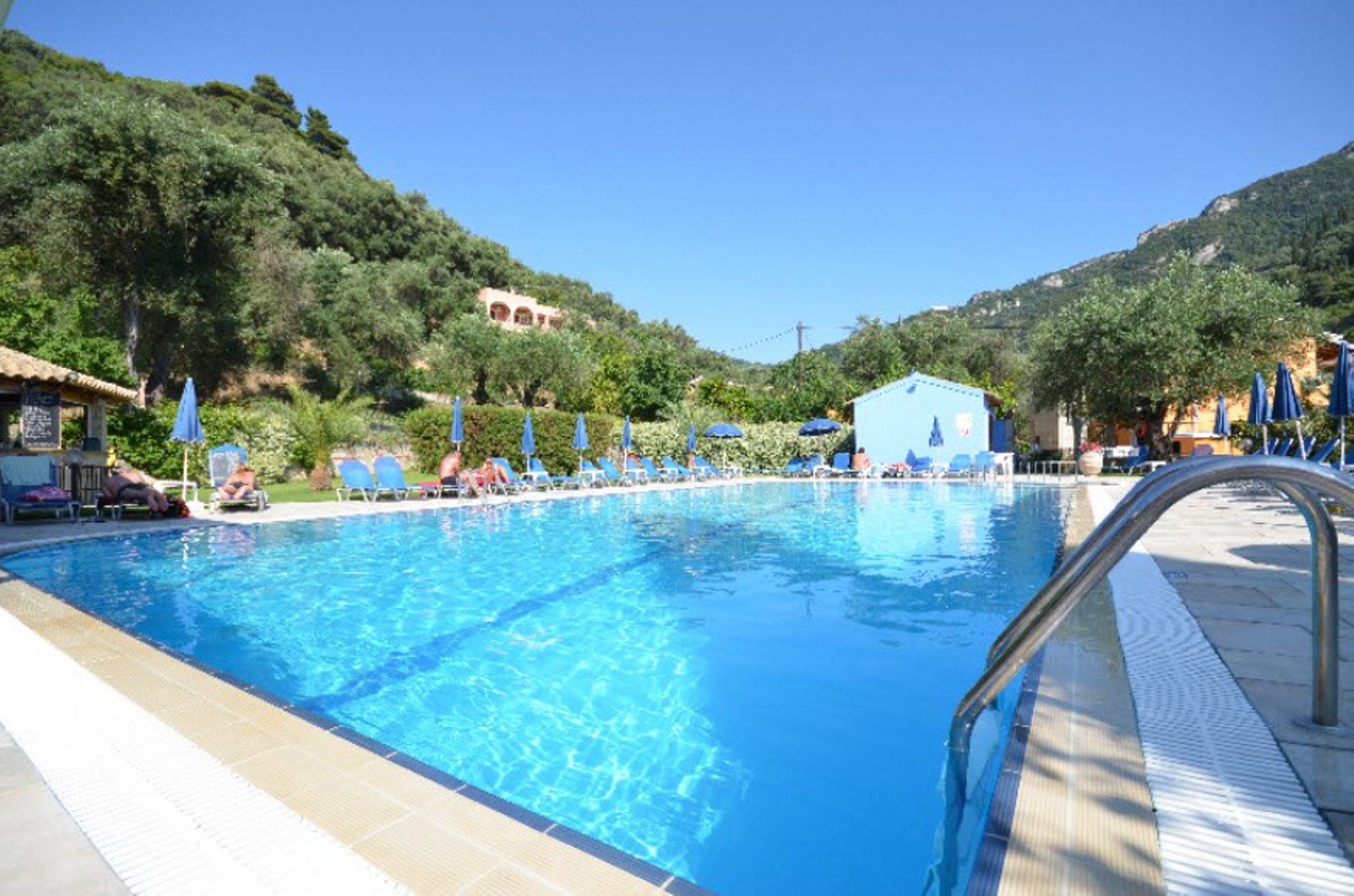 Une piscine à l’eau d’un bleu cristallin, entourée de chaises longues et de parasols, avec en toile de fond des collines et un ciel dégagé.