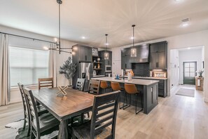 Una cocina moderna con una isla central, iluminación colgante y un comedor con sillas de madera.