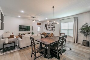 A modern living room with a dining area, a flat-screen TV, and a ceiling fan. - 🤠 Welcome to the Stockyards Stable: fire pit, walk to Stockyards & Billy Bob’s! (Fort Worth)