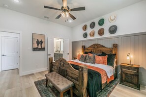 Un dormitorio con cama de madera, un banco, un ventilador de techo y una pared con sombreros.