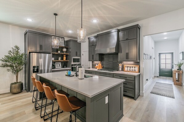 Una cocina moderna con una isla central, taburetes de bar y una lámpara colgante.