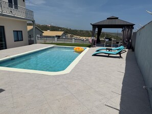 A swimming pool with a tiled deck, a gazebo, and lounge chairs.