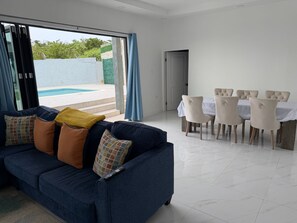 A modern living room with a blue sofa, a dining table with chairs, and a view of a swimming pool.