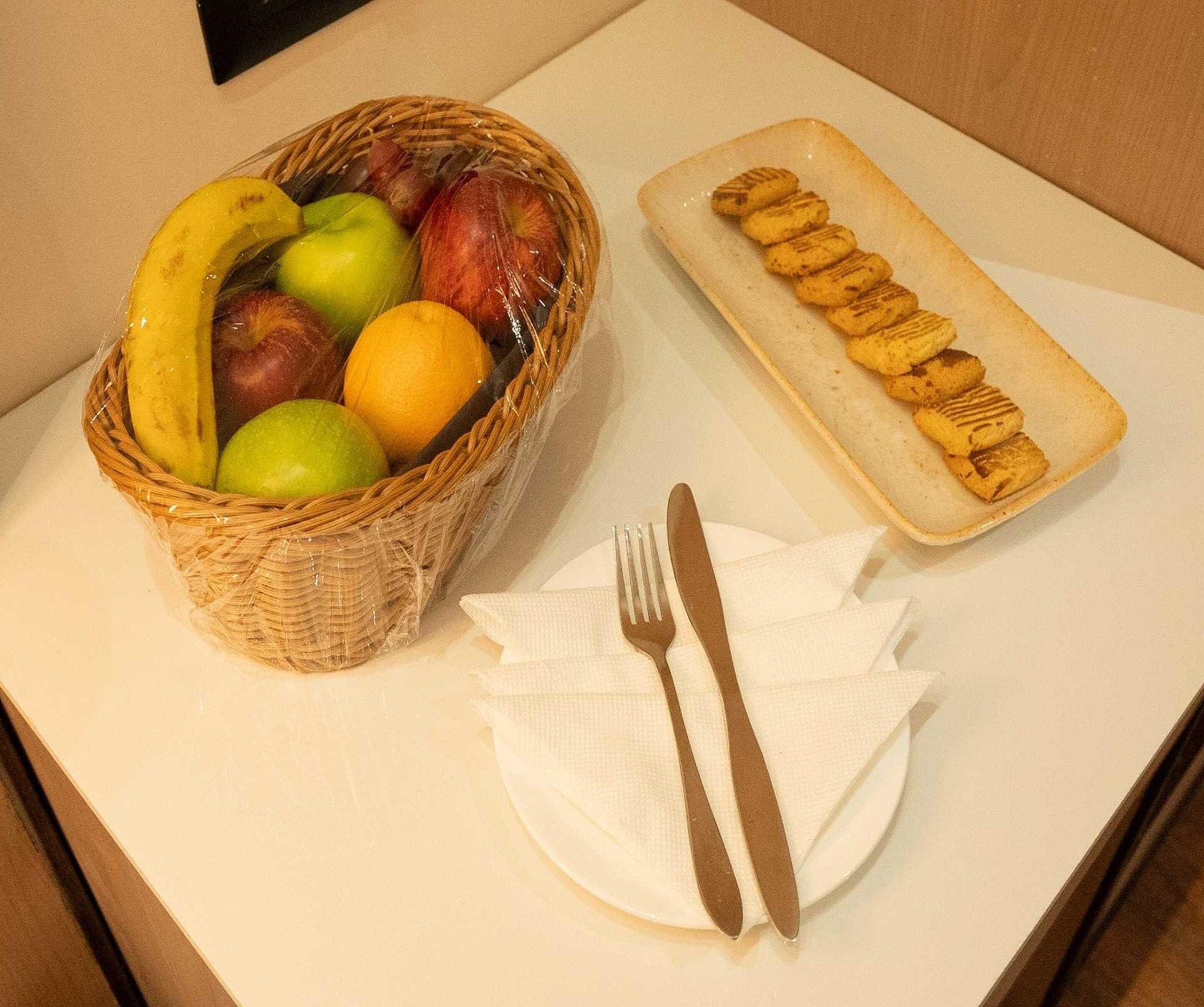 Une table avec un panier de fruits, une assiette de biscuits et des couverts.