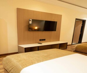 A hotel room with a bed, a bedside table, a TV mounted on a wooden panel, and a door.