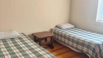 Une chambre avec deux lits, une petite table, un panneau en bois accroché au mur et une fenêtre avec des stores.
