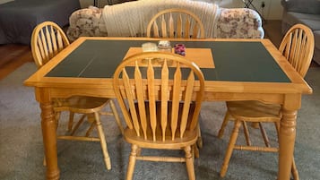 Un coin repas avec une table et des chaises en bois, un ventilateur de plafond, une horloge et un téléviseur posé sur un meuble.