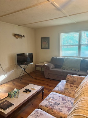 A living room with a television on a stand, a sofa, a coffee table, and a window with blinds.