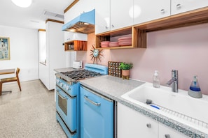 A kitchen with blue and white cabinetry, a gas stove, a sink, and a decorative clock. - Lido Beach House Family Complex (Sarasota)