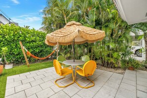 Eine Terrasse mit Tisch und Stühlen, einem Reetdachschirm und einer Hängematte.