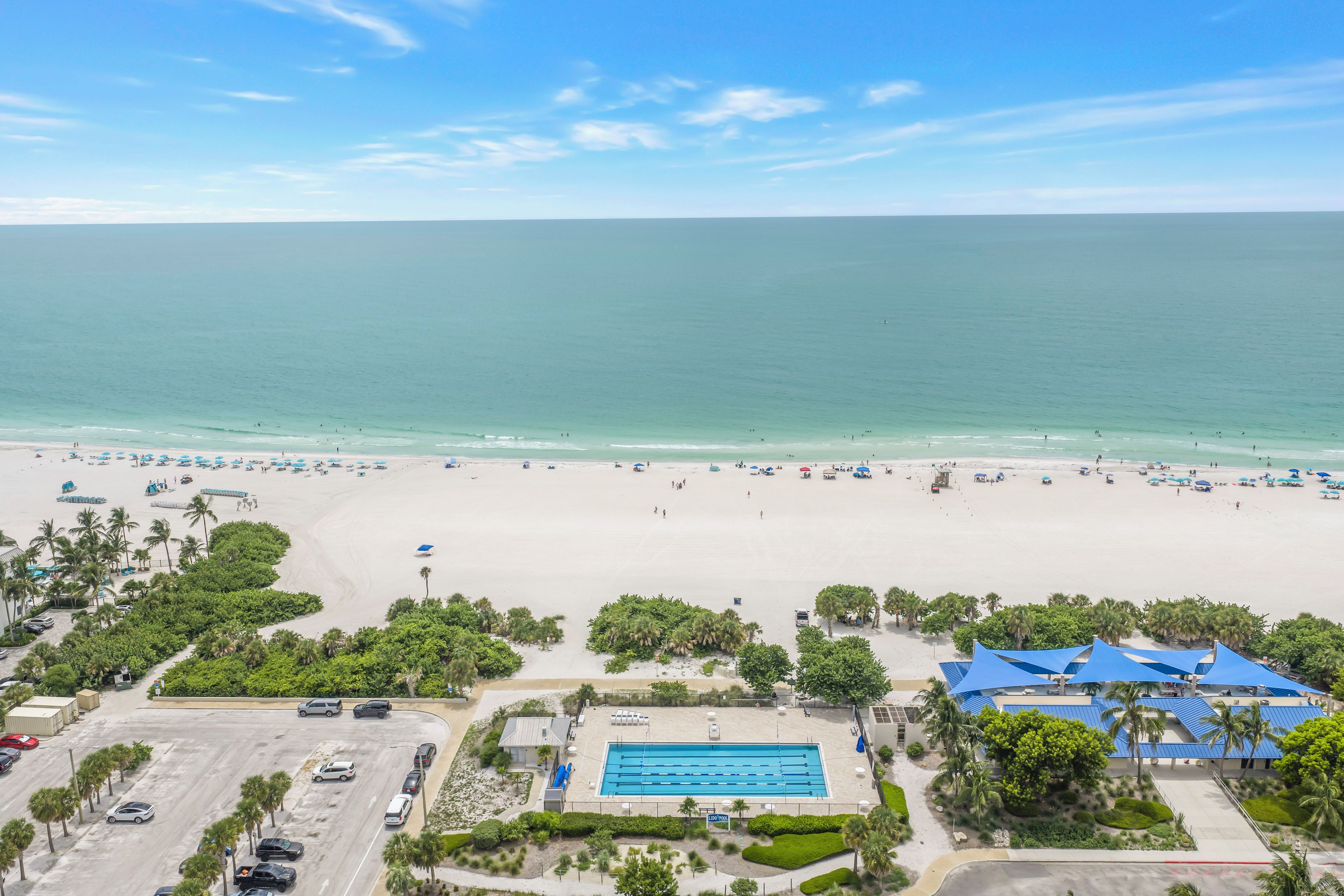 A beach resort with a swimming pool, beach umbrellas, and palm trees.