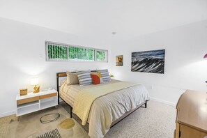 A bedroom with a bed, a nightstand, a lamp, a window with a view of greenery, and a painting of a wave. - Lido Beach House Family Complex (Sarasota)