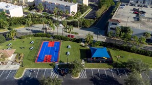 Vue aérienne d’un parking avec un terrain de basket, un espace de repos couvert et des espaces verts environnants.