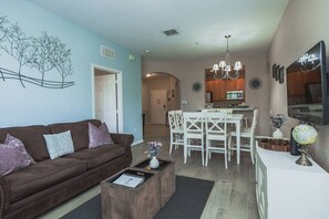 A living room with a brown sofa, a coffee table, and a dining area with white chairs and a chandelier. - Vista Cay 3BR near Universal & Convention (Orlando)