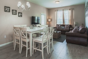 A dining area with a white table and chairs, a flat-screen TV, and a chandelier. - Vista Cay 3BR near Universal & Convention (Orlando)