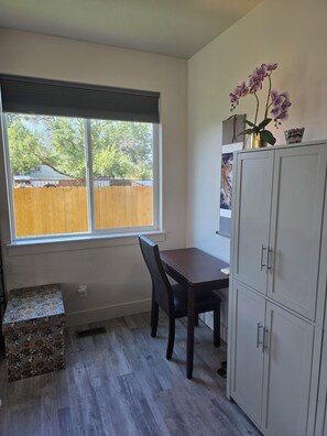Ein Zimmer mit Fenster, Tisch, Stuhl, Schrank und einer kleinen Dekoration auf der Fensterbank.