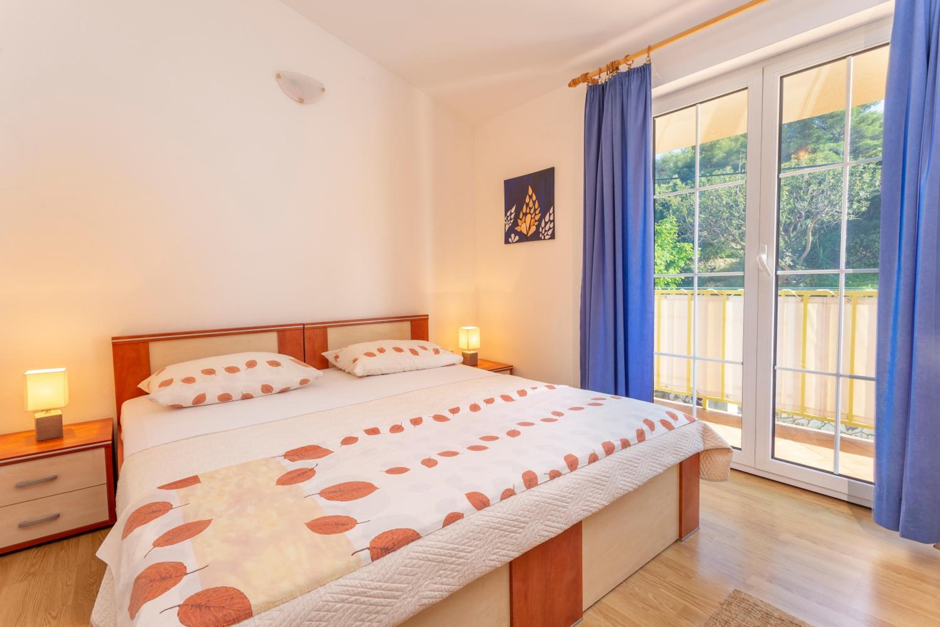 Un dormitorio con cama, mesitas de noche, ventana con cortinas y vistas a zonas verdes.