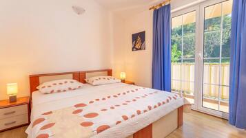 Un dormitorio con cama, mesitas de noche, ventana con cortinas y vistas a zonas verdes.