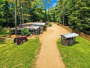 A rural property with a gravel driveway, a red tractor, a wooden shed, and a fenced area.