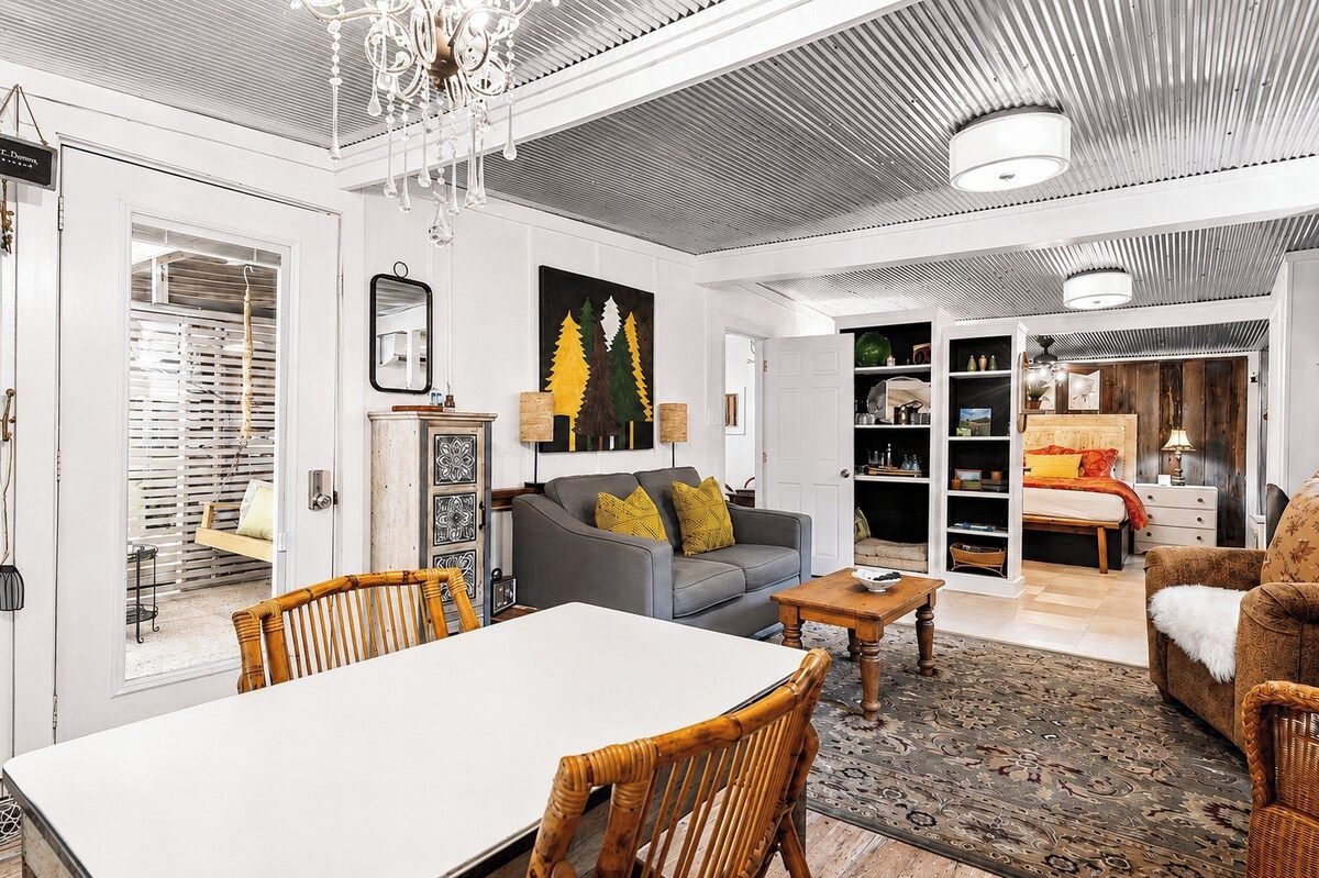 Un salon comprenant un canapé, une table à manger et des chaises. On y trouve également un lustre, une cheminée et une bibliothèque.