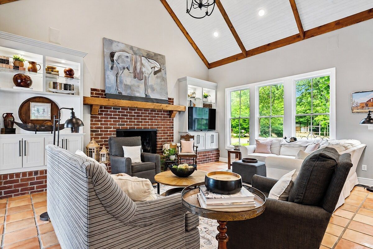 A living room with a fireplace, a sofa, a coffee table, and a view of greenery outside.