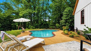 A swimming pool with a curved edge, surrounded by a garden with trees and shrubs. There are lounge chairs and a table with a tablecloth. - The Acres, 4BR Farm Stay by Velvet Ditch Villas (Oxford)