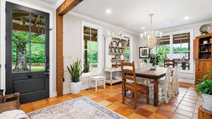 A dining area with a wooden table and chairs, surrounded by white walls and a large window. - The Acres, 4BR Farm Stay by Velvet Ditch Villas (Oxford)