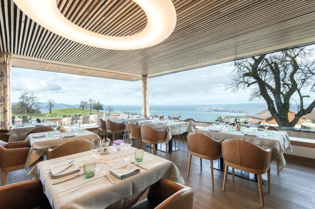 Ein Restaurant mit gedeckten Tischen, Blick auf das Meer und einem großen Baum davor.