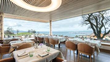 Ein Restaurant mit gedeckten Tischen, Blick auf das Meer und einem großen Baum davor.