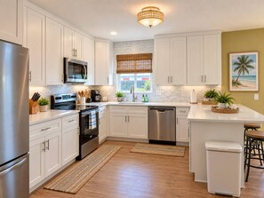 A modern kitchen with white cabinetry, stainless steel appliances, and a central island with stools.