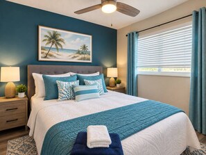 A bedroom with a bed, a ceiling fan, a nightstand with a lamp, and a window with curtains.