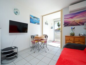 A room with a dining table, chairs, a TV, a clock, a vase, and a painting. - Seaside Apartment in Cap D'agde (Agde)