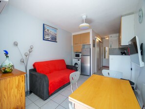 A compact living space with a sofa, a dining table, a washing machine, and a refrigerator. - Seaside Apartment in Cap D'agde (Agde)