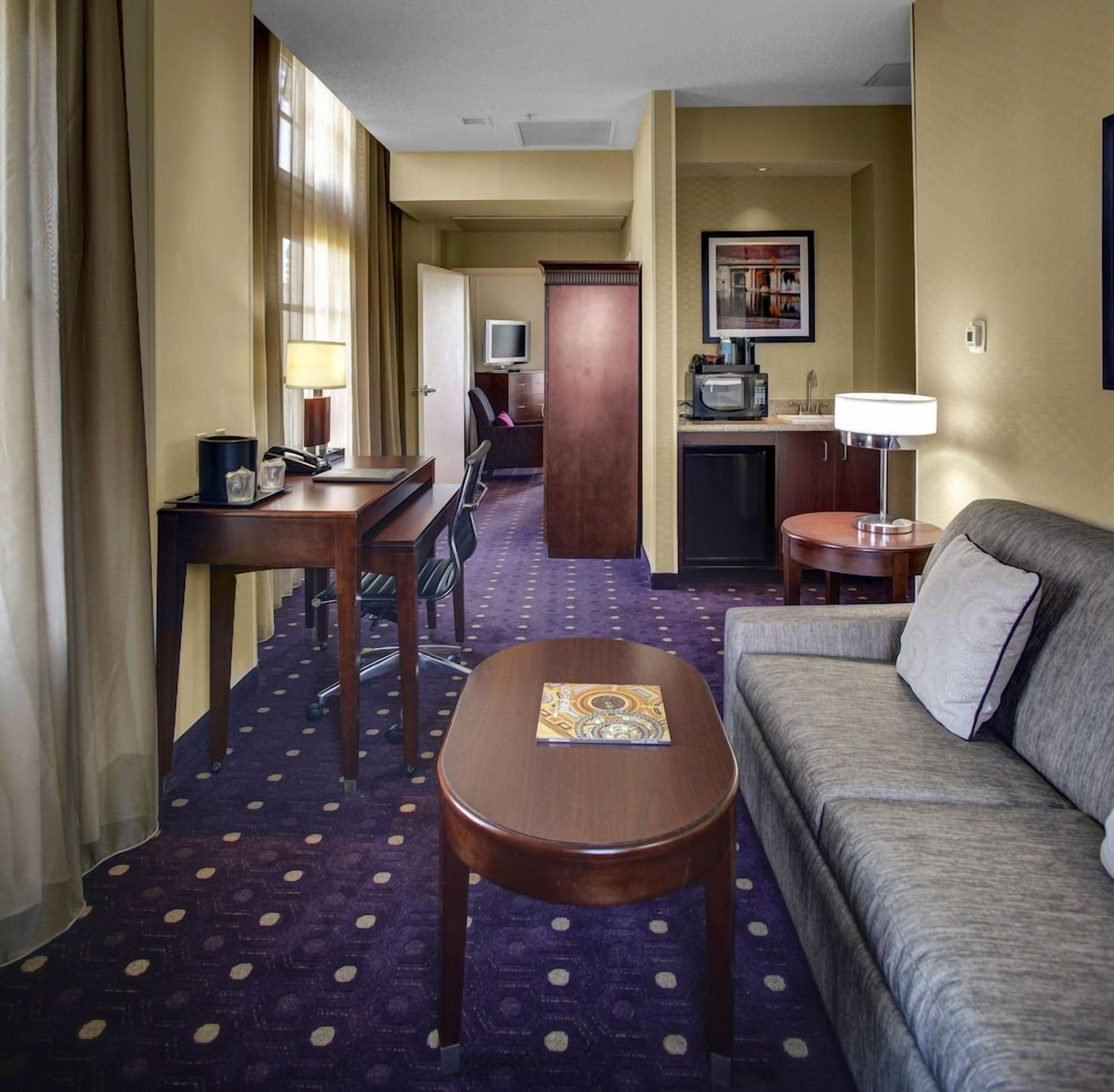 Une chambre d’hôtel équipée d’un canapé, d’une table ronde, d’un bureau avec une chaise, d’une kitchenette et d’un téléviseur.